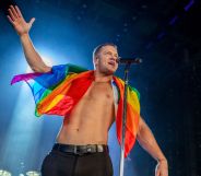 Imagine Dragons frontman Dan Reynolds performs shirtless on stage with an LGBTQ+ flag wrapped around his shoulders.