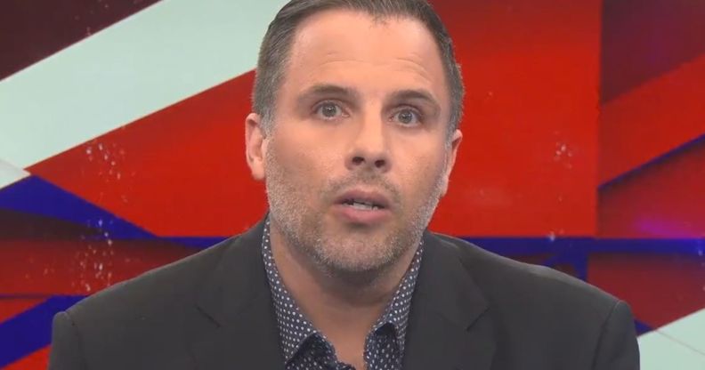 Dan Wootton, on the set of GB News, speaks towards a camera while wearing a suit and open collar shirt.