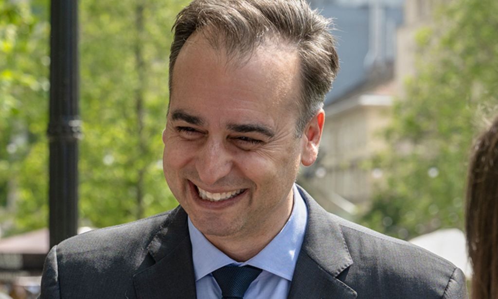 David Pressman smiles at an unpictured individual in a park while wearing a suit and tie.