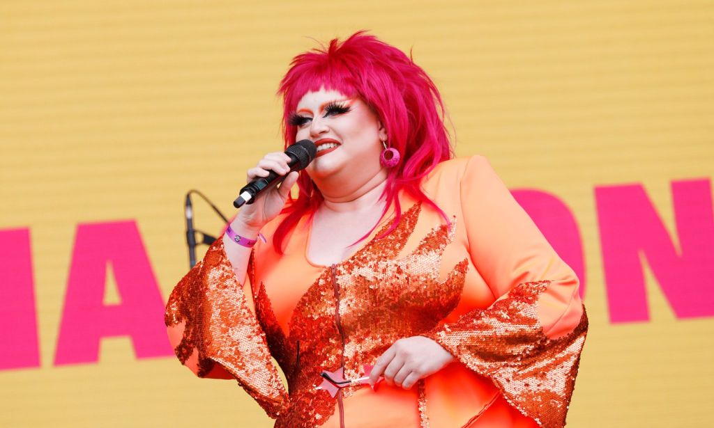 Drag Race star Victoria Scone in an orange outfit and red wig speaking to the crowd at Pride in London 2022.