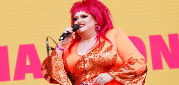 Drag Race star Victoria Scone in an orange outfit and red wig speaking to the crowd at Pride in London 2022.