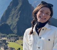 Dylan Mulvaney smiles, while wearing a white jacket, looking over the Peruvian mountains.