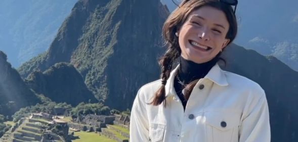 Dylan Mulvaney smiles, while wearing a white jacket, looking over the Peruvian mountains.
