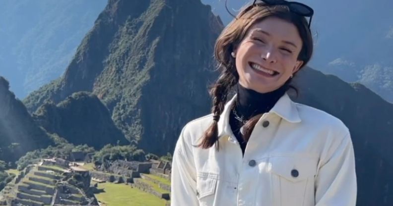 Dylan Mulvaney smiles, while wearing a white jacket, looking over the Peruvian mountains.