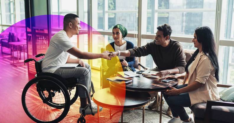 This is an image of a man in a wheelchair shaking another mans hand. There are two women smiling. They are in a bright and airy office.