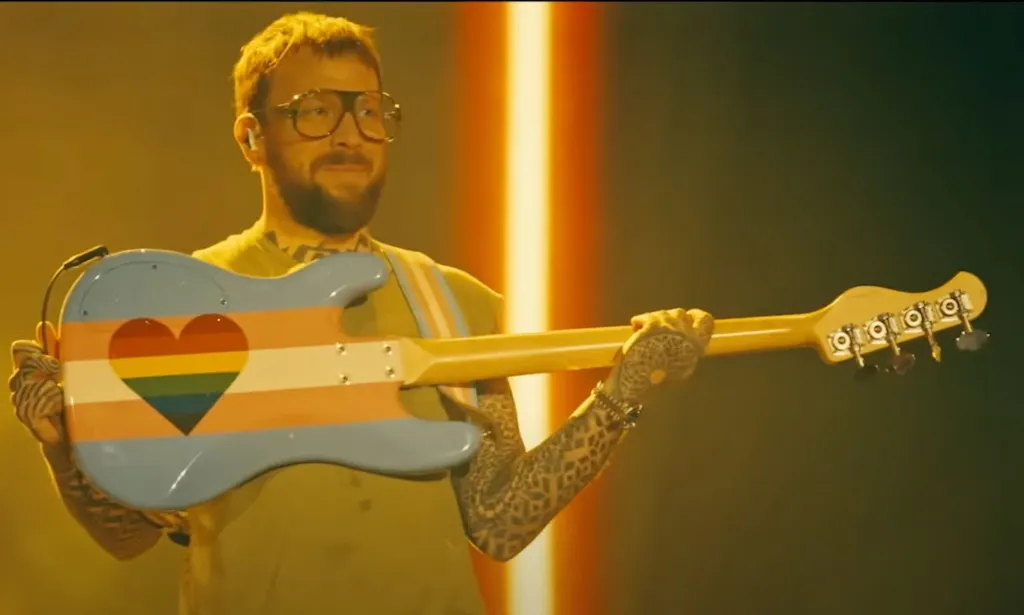 Ben McKee of Imagine Dragons holds up a guitar painted in the trans flag colours.