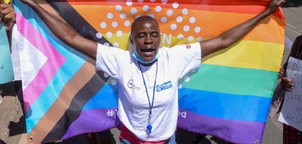 A Kenya LGBTQ+ activist holds up a Progress Pride flag behind them.