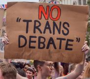An individual holds up a cardboard sign that reads "No Trans Debate" during a Pride parade.
