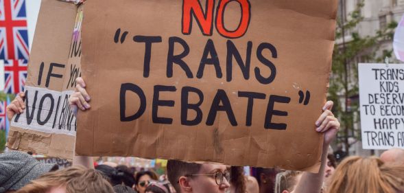 An individual holds up a cardboard sign that reads "No Trans Debate" during a Pride parade.