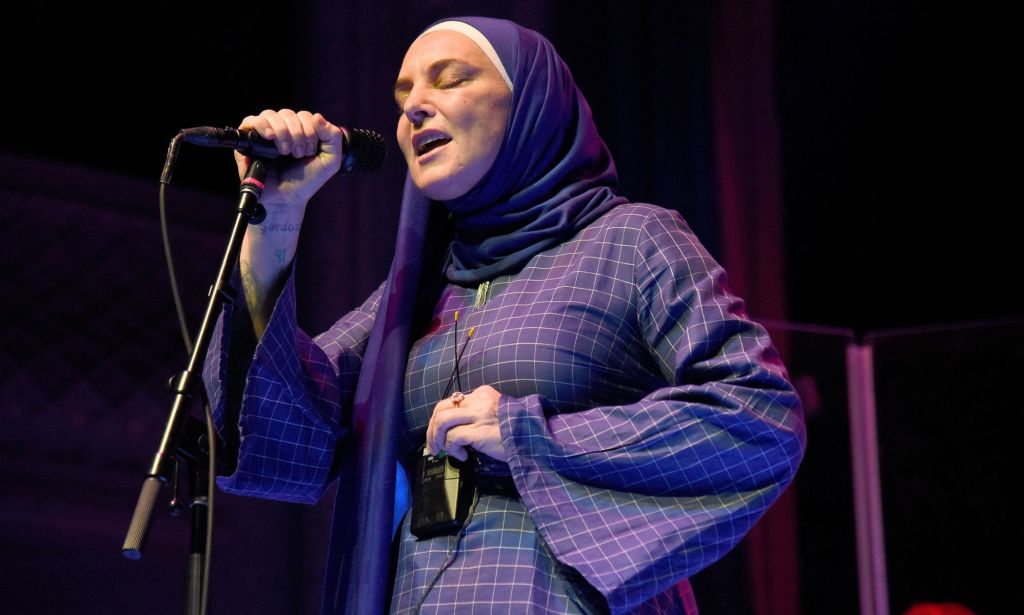 Sinéad O’Connor in a hijab, sings into a microphone.