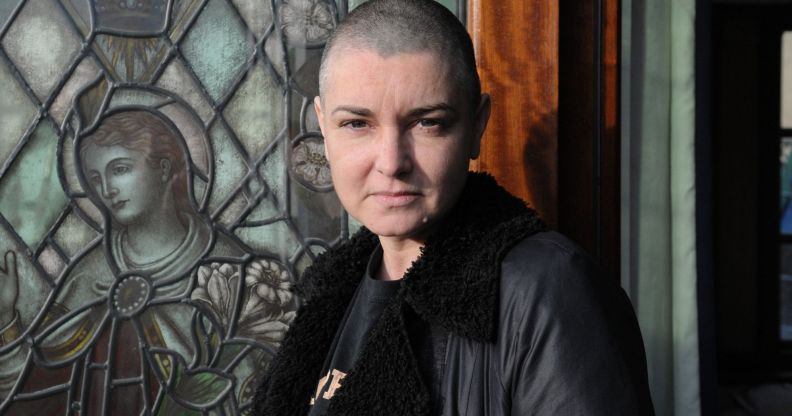 Sinead O'Connor wears a black top and jacket while standing in front of a front door.