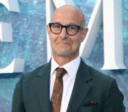 Stanley Tucci at the UK premiere of The Little Mermaid, wearing a green suit and red tie with black rimmed glasses.