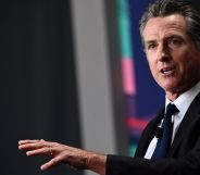California governor Gavin Newsom wears a suit and tie as he gestures off screen, he recently threatened to fine a school district for not using materials mentioning Harvey Milk