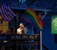 Residents drink on the balcony of a restaurant as the sun goes down, while a Pride and US flag wave.