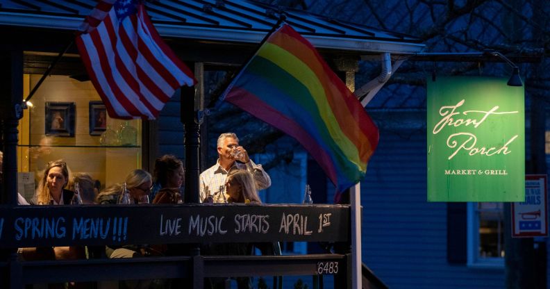 Residents drink on the balcony of a restaurant as the sun goes down, while a Pride and US flag wave.