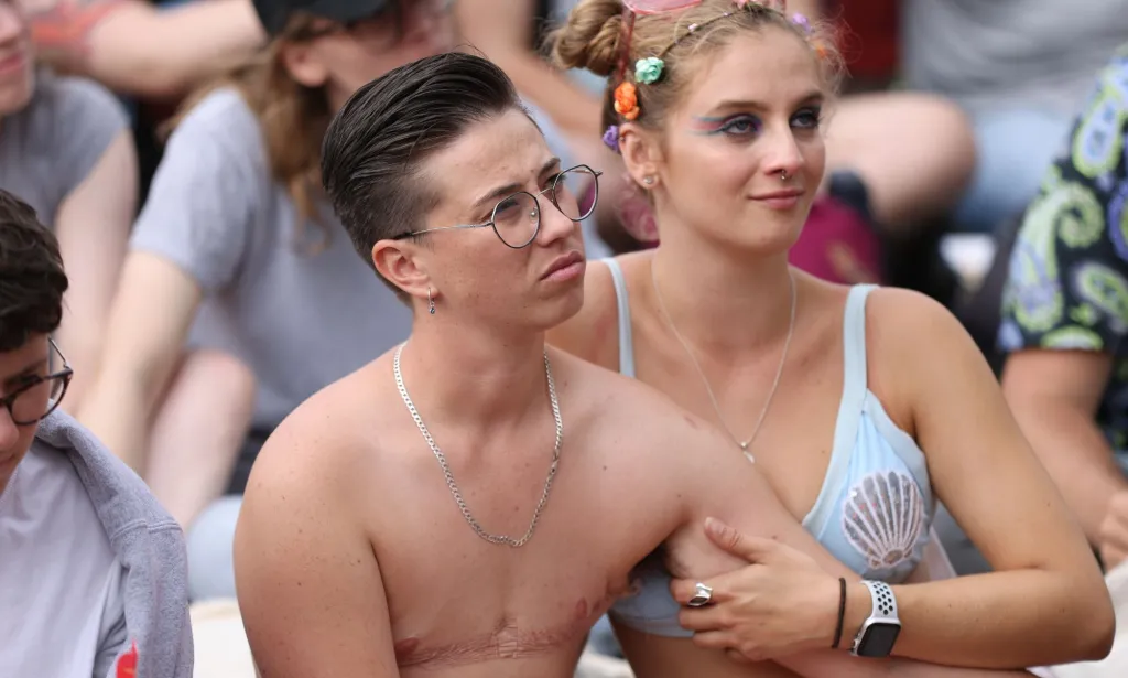 Two people sit down in a crowd during a Pride parade.