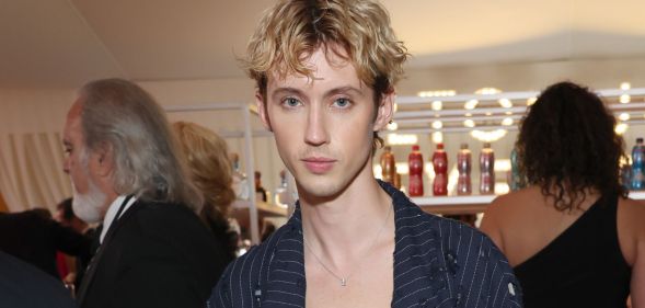 Troye Sivan wears a black pinstriped blazer and low cut top.