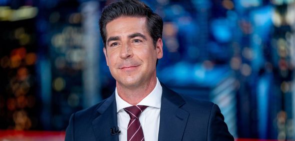 Fox News host Jesse Watters wears a suit and tie and sits at a desk