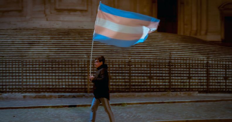 Person carries a large trans flag down the street
