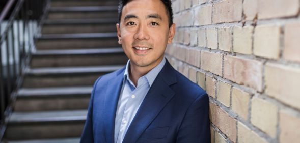 This is an image of Wayne Ting, the ceo of Lime. He is leaning on a brick wall. He is wearing a dark blue blazer with a light blue shirt He has black hair.