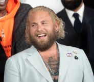 Jonah Hill, a white man with long bleached hair, wearing a light blue suit reveaing his tattooed chest