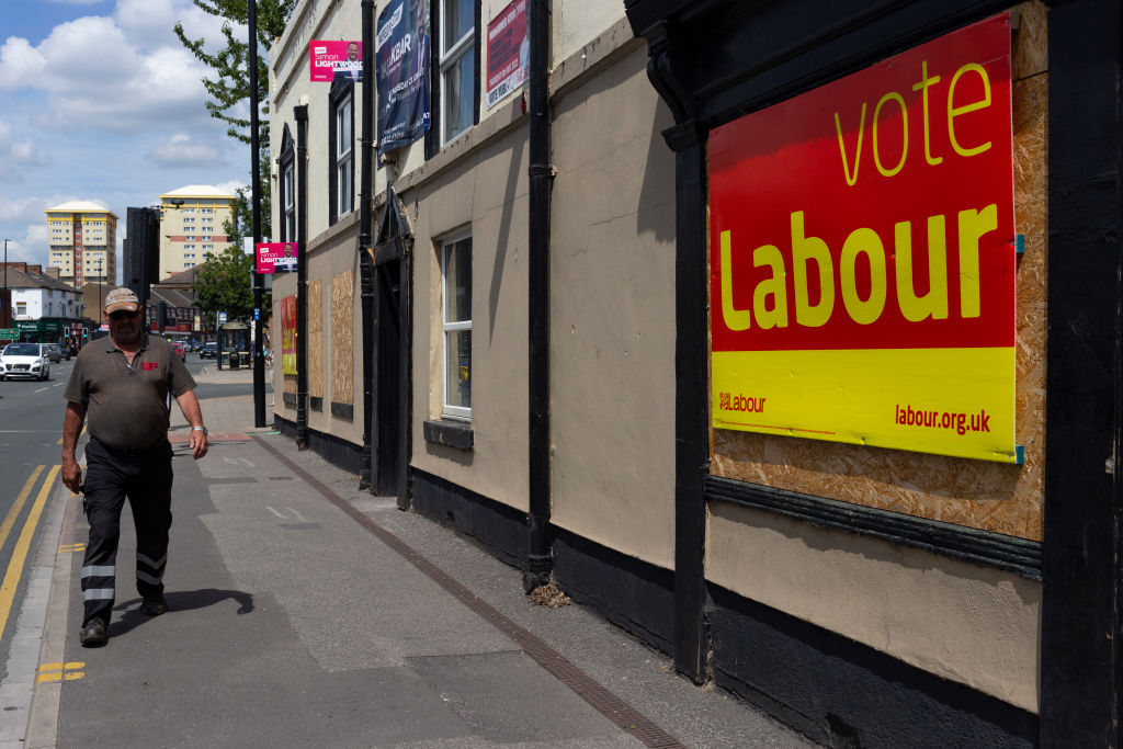 A member of the public makes their way past a vacant pub with several placards and signs campaigning for the Labour Party as voters in the former Red Wall constituency prepare to cast their ballots in a by-election. 