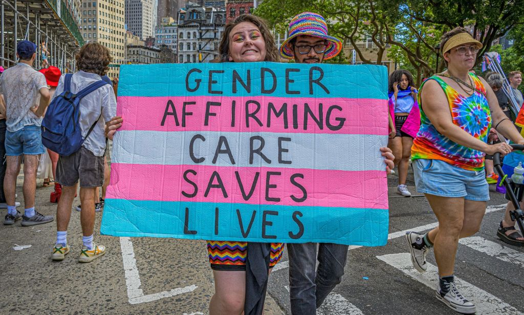 A person holds up a sign during an LGBTQ+ demonstration that reads 'gender-affirming care saves lives' in the colours of the trans pride flag