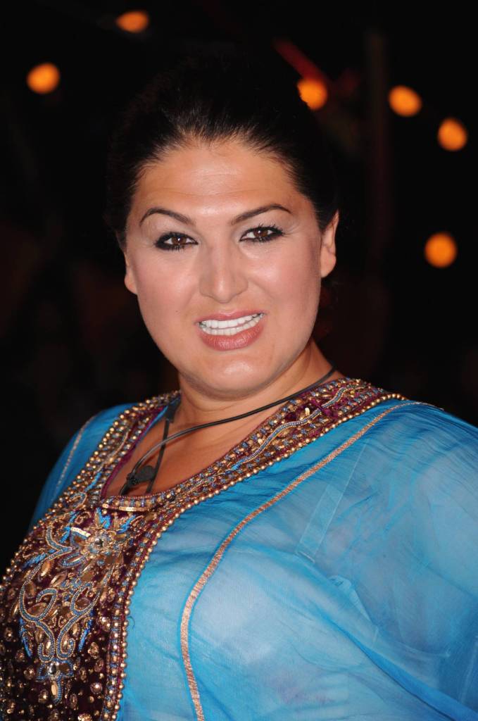 A photo of Big Brother winner Nadia Almada wearing a blue dress with embroidery on the chest as she smiles at the camera