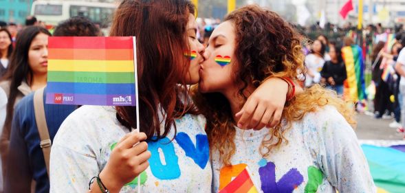 A couple kiss as they hold up rainbow LGBTQ+ Pride flags during a march in Peru where advocates call for same-sex marriage laws, for queer people to be protected from discrimination and more