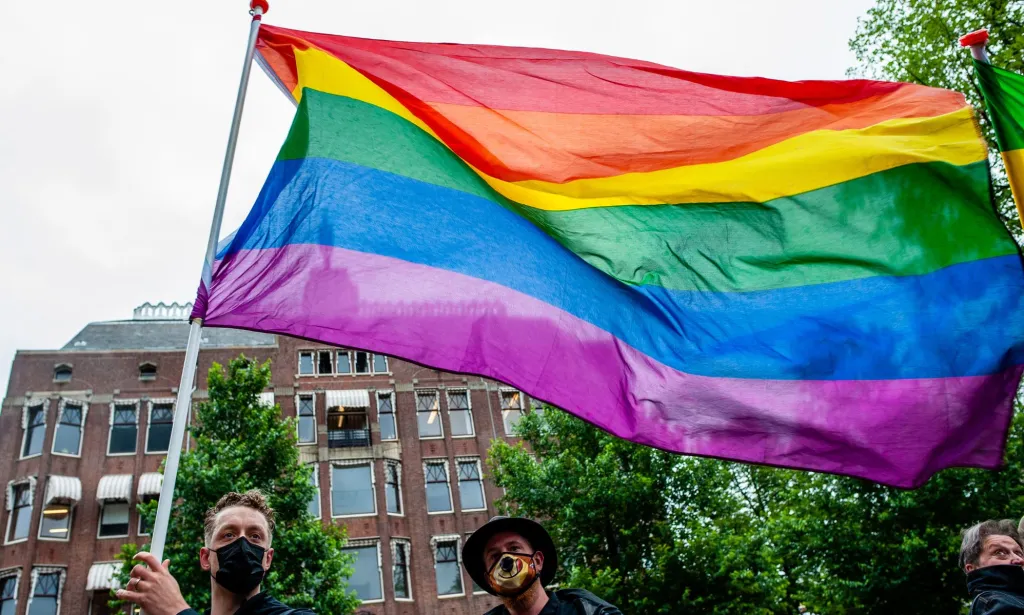 A person holds up a rainbow LGBTQ+ Pride flag 
