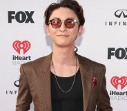 Shinjiro Atae, in a brown suit and red glasses, smiles on a red carpet.