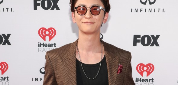Shinjiro Atae, in a brown suit and red glasses, smiles on a red carpet.