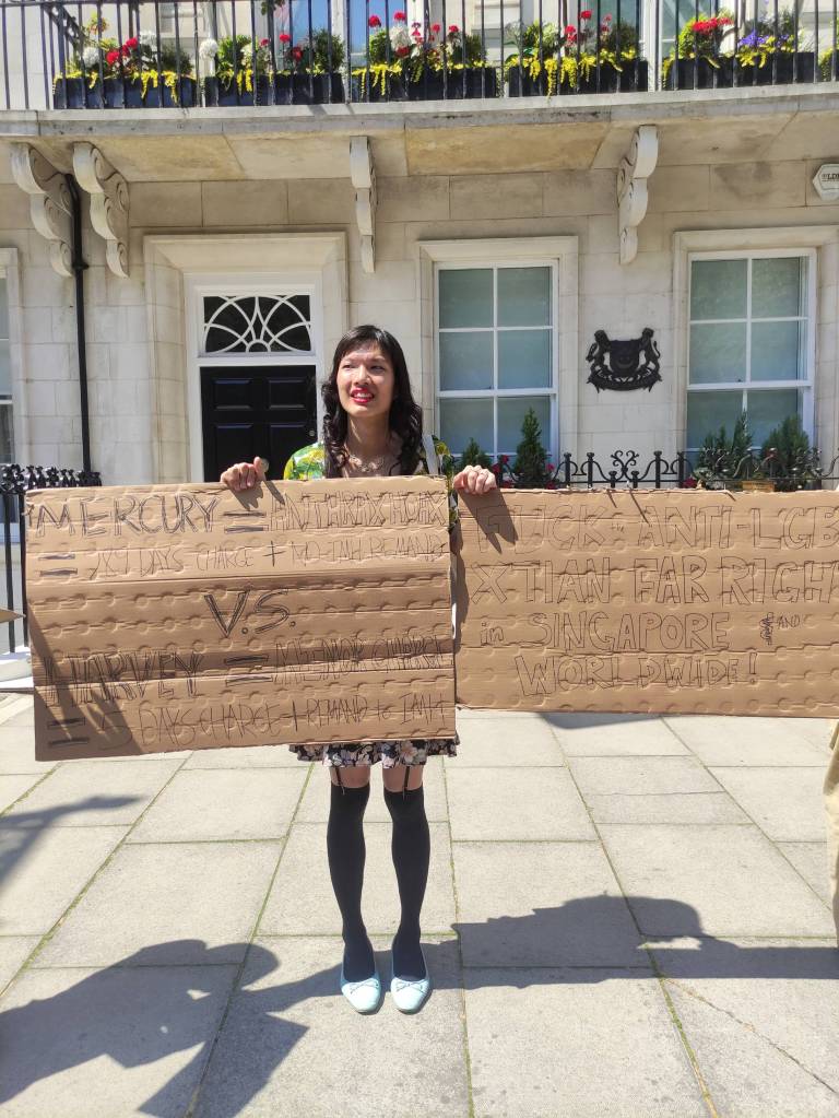 Trans woman Lune Loh holds up two cardboard signs outside the Singapore High Commission in London, UK during a protest denouncing attacks she's faced as a trans person as well as anti-LGBTQ+ persecution in Singapore