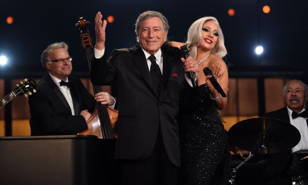 Singer Tony Bennett waves to the crowd as he hugs Lady Gaga, who is holding a microphone, during a concert