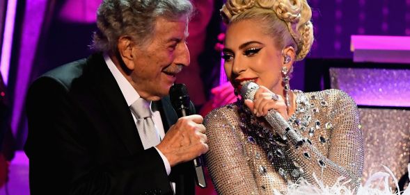 Tony Bennett and Lady Gaga sit side by side as they sing into microphones during a concert together