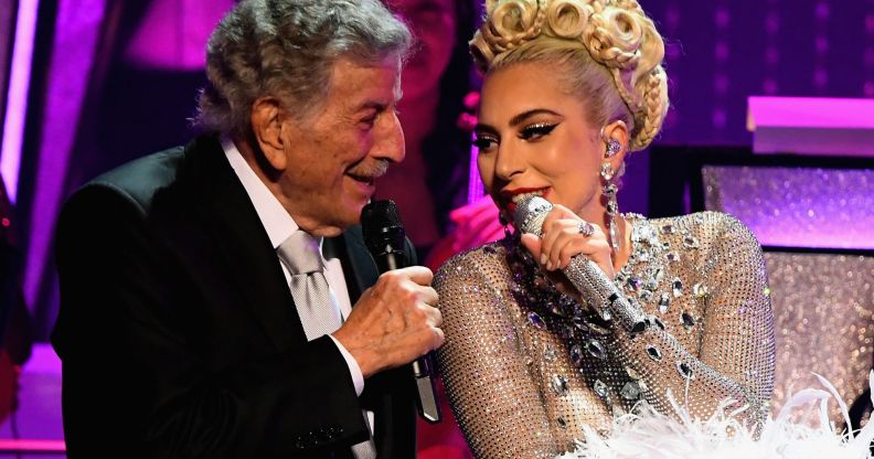 Tony Bennett and Lady Gaga sit side by side as they sing into microphones during a concert together
