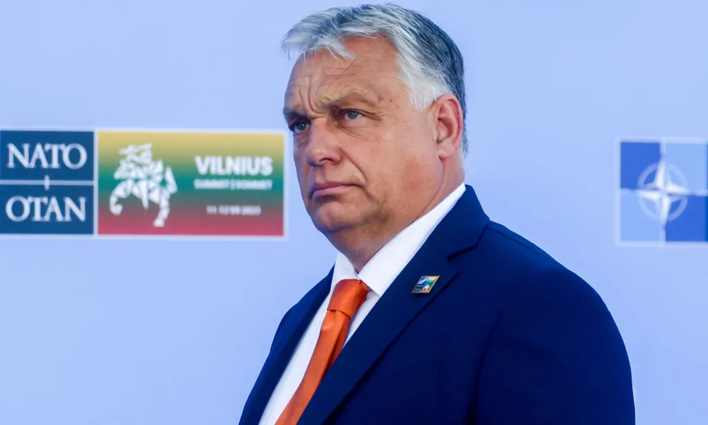 Hungary's prime minister Viktor Orbán, who has led an anti-LGBTQ+ regime, wears a white shirt, orange tie and blue jacket as he stares somewhere off camera