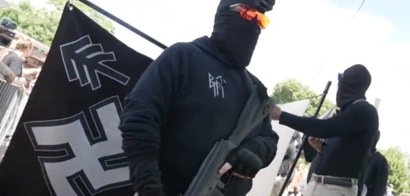 Nazi group member carrying a gun, in front of a Swastika flag