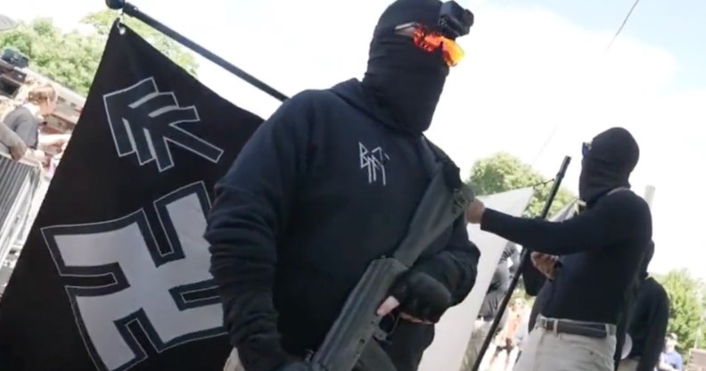 Nazi group member carrying a gun, in front of a Swastika flag