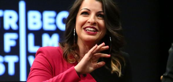 Anita Sarkeesian, in a black and pink dress, speaks at an event.