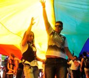 Crowds celebrate during a Brazil Pride march under a giant LGBTQ+ flag.