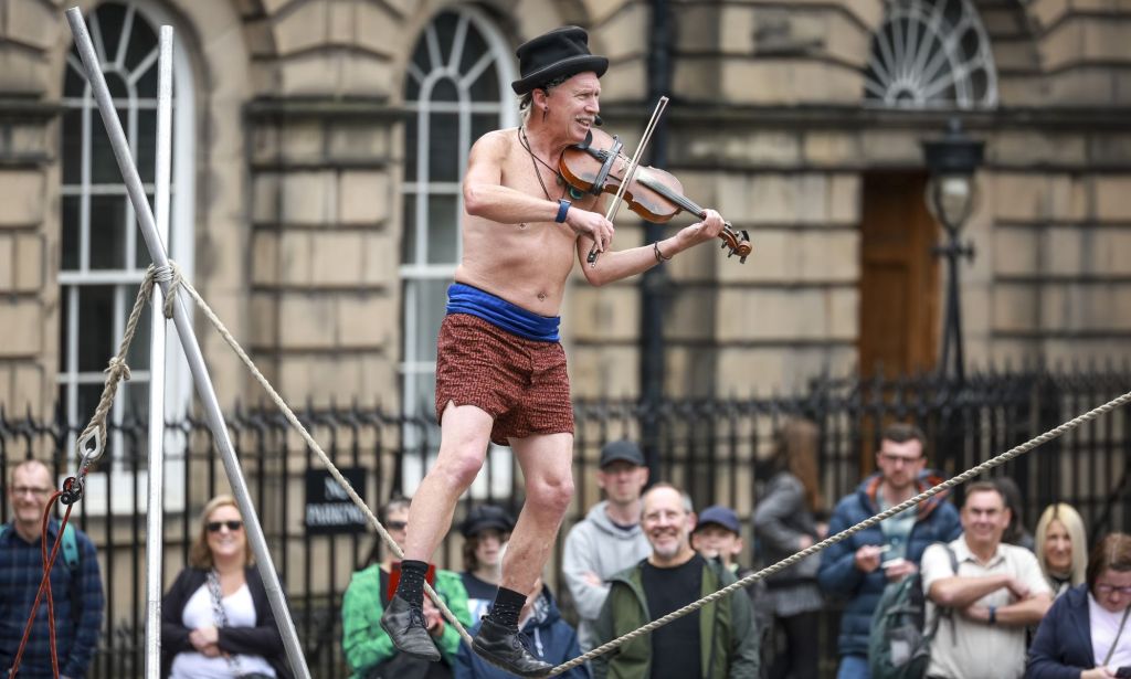 A man at Edinburgh Fringe Festival plays the violin while walking a tight rope.