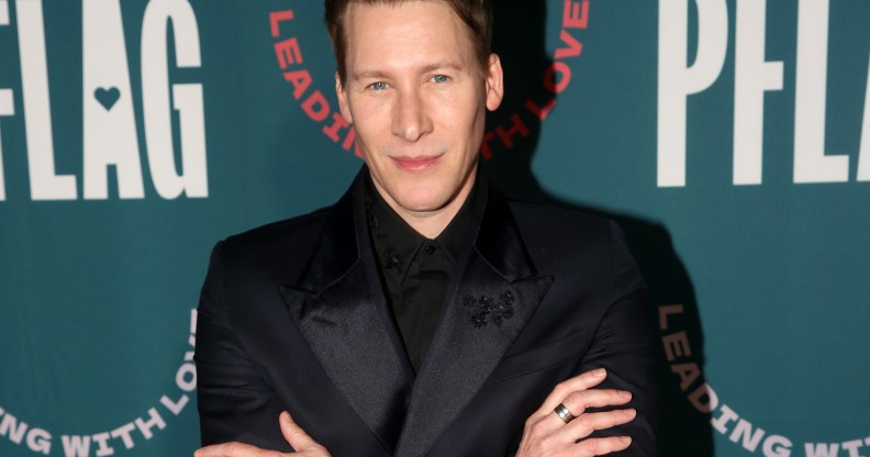 Dustin Lance Black poses on the red carpet in a black suit and shirt