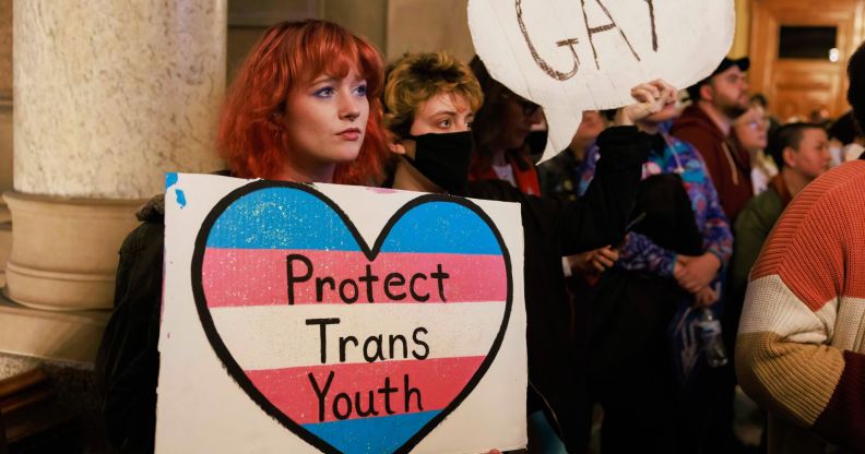 A protestor holds up a card reading "protect trans youth"