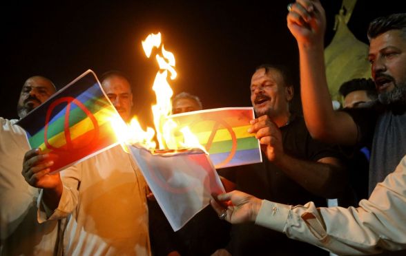 Homophobic protestors in Iraq burn pictures of the LGBTQ+ Pride flag.