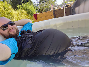 Jacob Stokoe during one of his pregnancies. In this image, they are pictured lying in a pool wearing a t-shirt with a baby bump visible through their shirt.