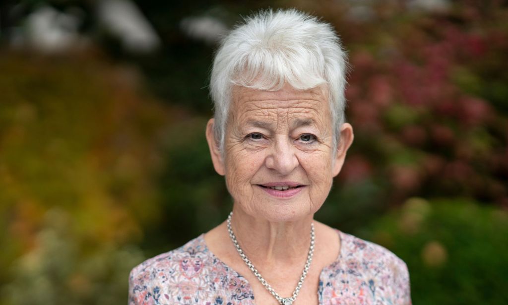 Jacqueline Wilson in a pink, white and purple flowery top and a silver necklace. Her hair is white and cropped short.