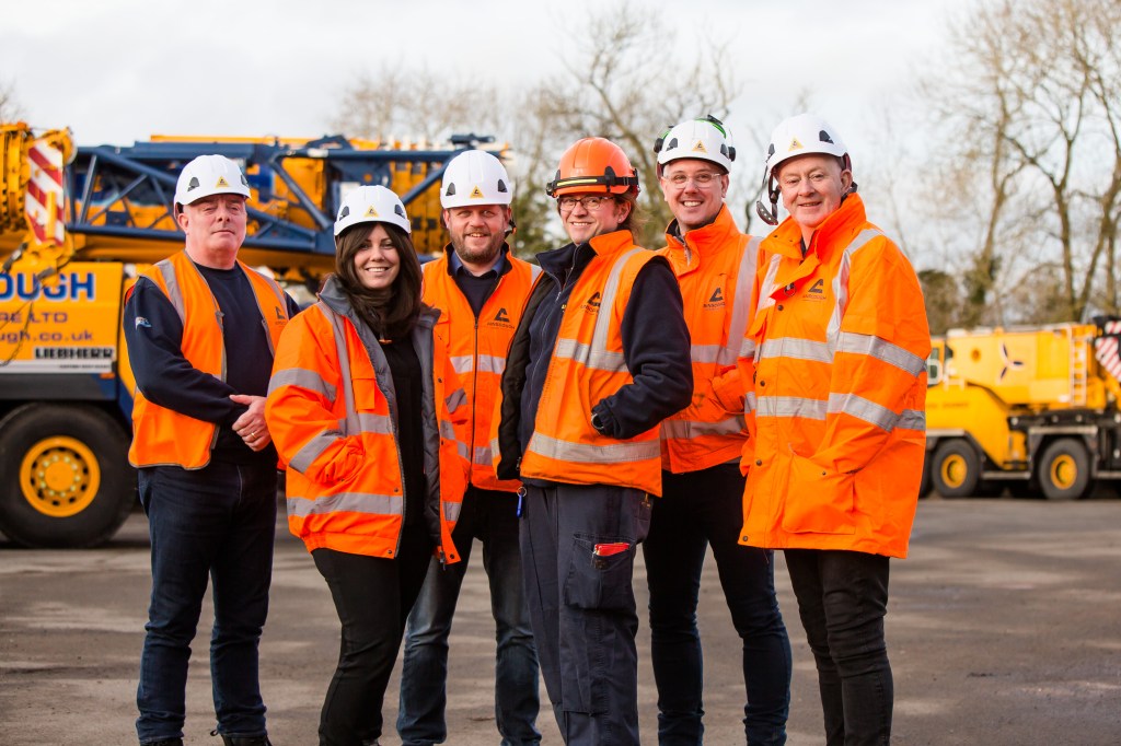 This is an image of 6 people on an HS2 construction site, including trans woman Kat. They are all wearing hard hats and orange hi-vis jackets.