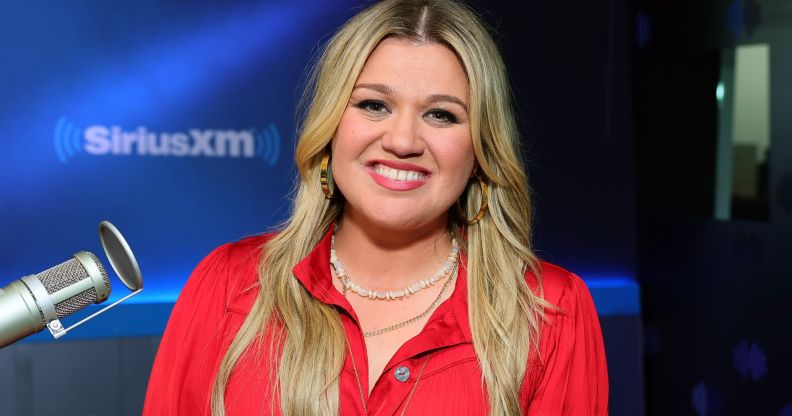Kelly Clarkson smiling during a radio appearance. She is wearing a red shirt and two necklaces.