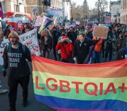 Protestors march through a street with pro-LGBTQ+ flags.